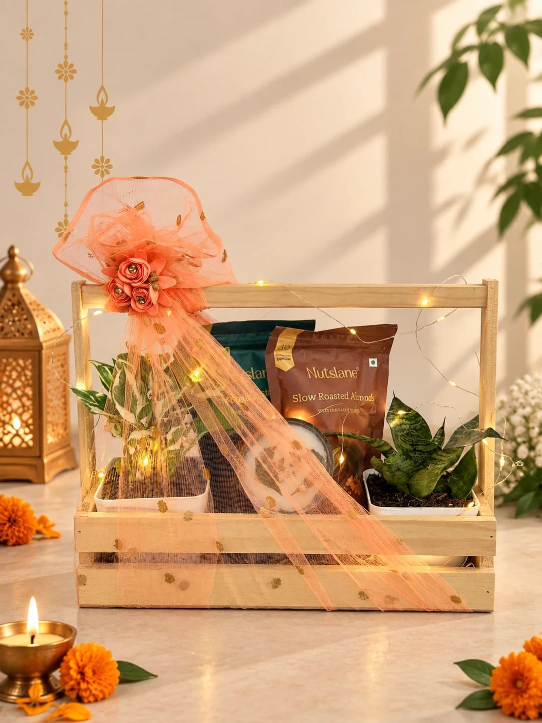 Wooden gift carrier with two potted plants and snack packets, decorated with peach ribbon and string lights.